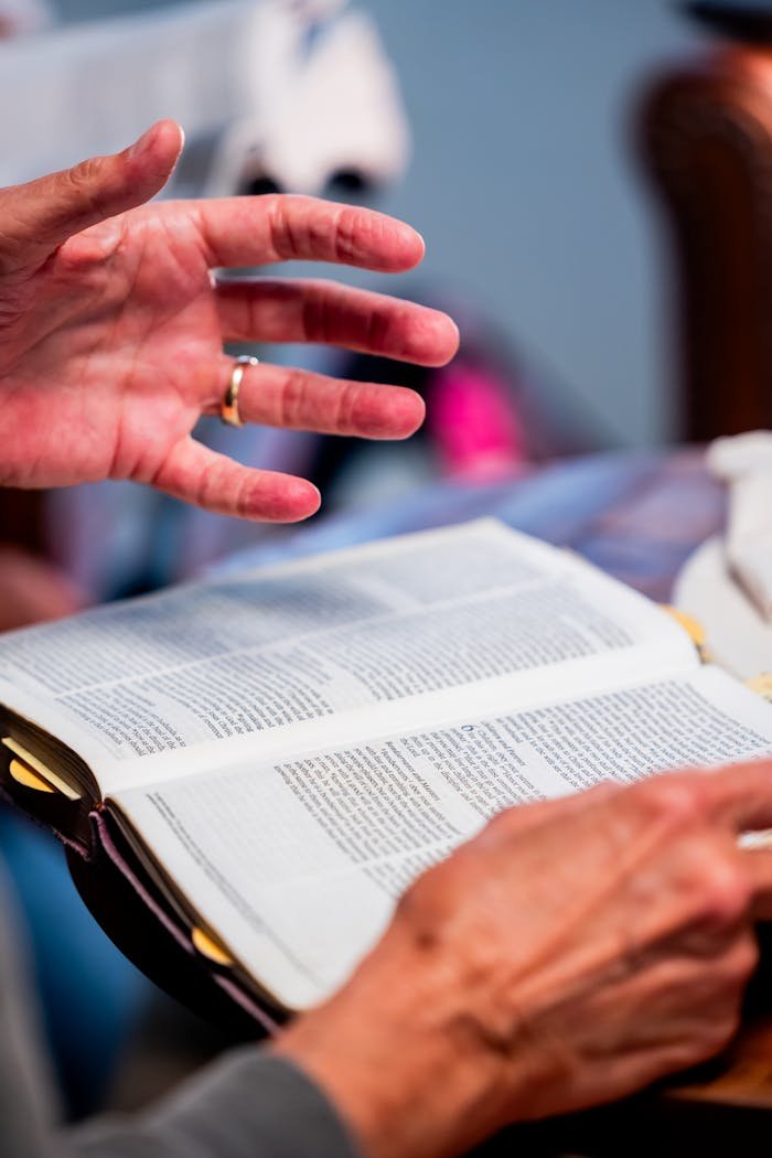 Contact Close-up of hands engaged in Bible study at an indoor setting, promoting spiritual discussion.