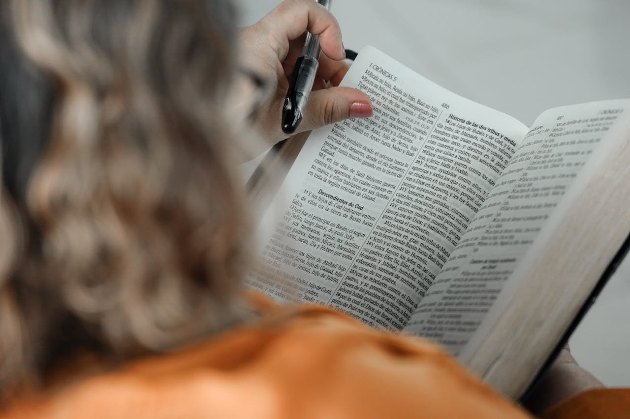 Close-up of a woman reading a Bible with a pen, focused on text.